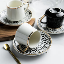 Lade das Bild in den Galerie-Viewer, Kaffeetasse mit Unterteller in schwarz-weißen Muster und goldenen Akzenten inkl. goldenem Löffel
